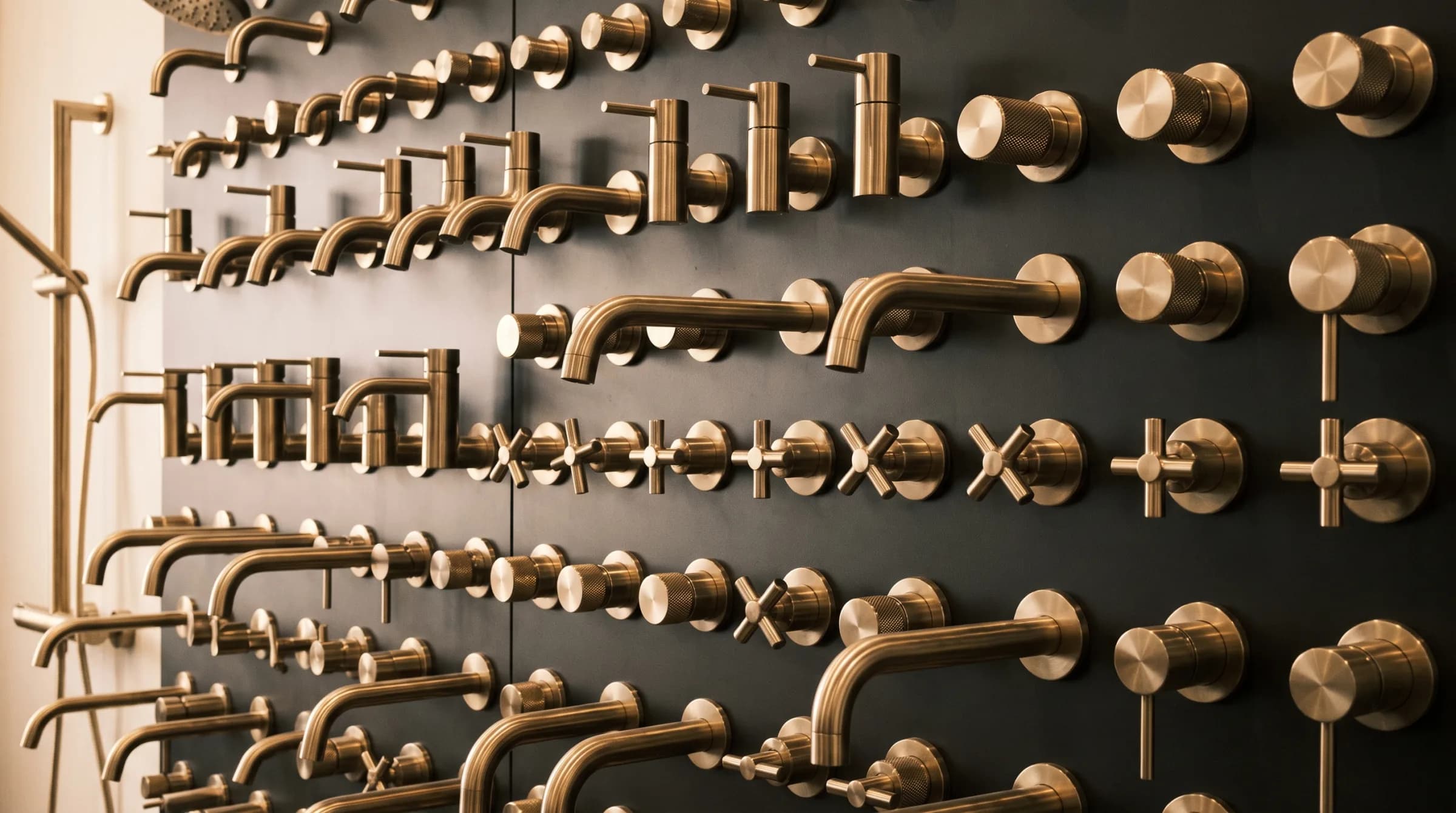 A wall of aged brass bathroom brassware and fittings, each piece catching low raking light